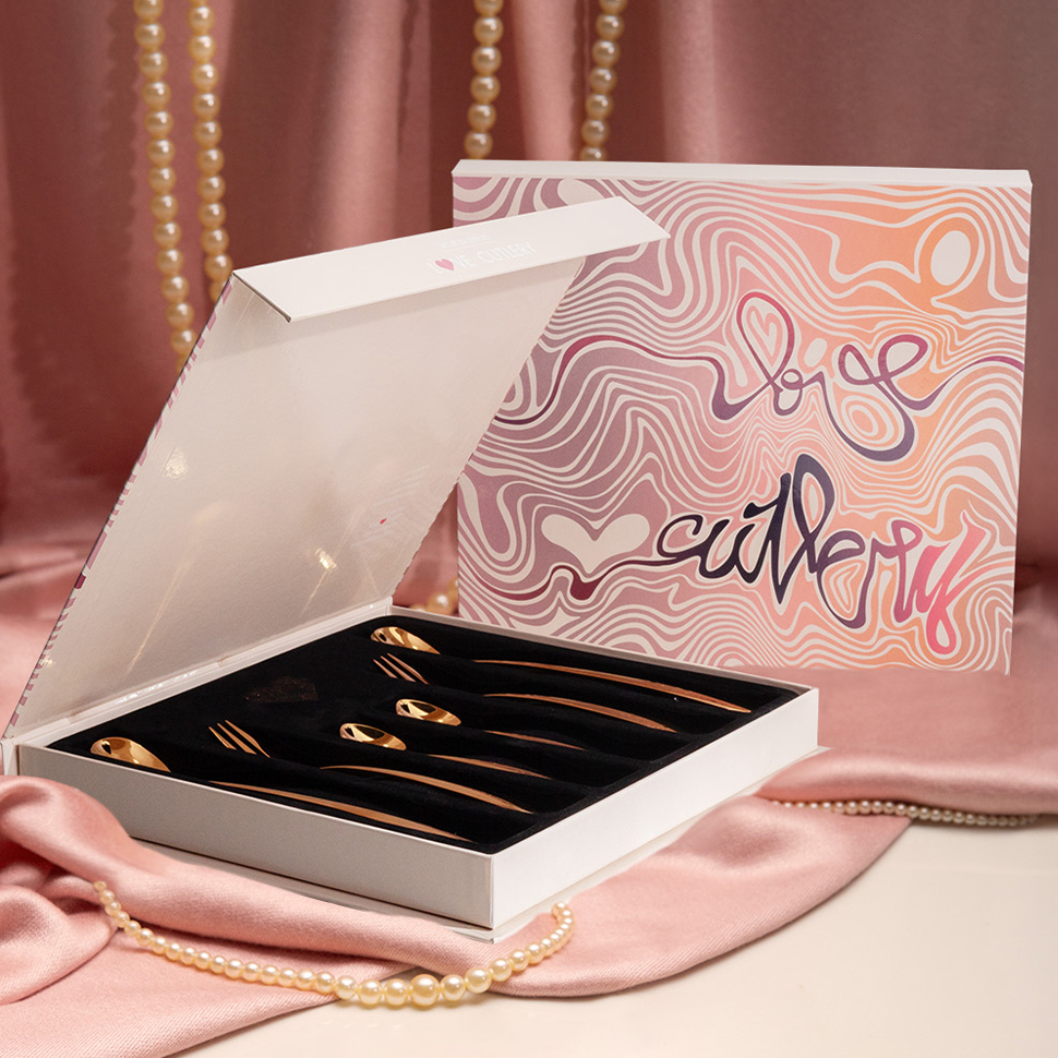 Odprta bela škatla z zlatimi žličkami Love Cutlery, položena na rožnat saten 